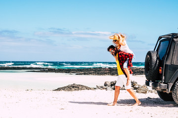 Happy caucasian people couple have fun together at the tropical white sand beach with blu eocean and sky in background - off road car parked and concept of travel with vehicle © simona