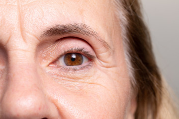 An extreme closeup view on the eye of an elderly woman with brown iris. Heavy wrinkles and laughter...