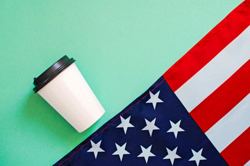American flag and coffee paper cup on green background.