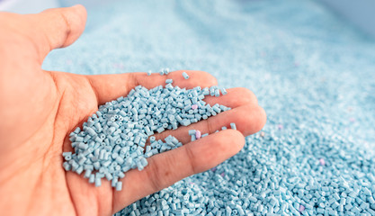 Hand on large pile of blue plastic granules in temporary storage of production line at recycle factory, masterbatch dye polymer plastics resin pellet background,  injection molding process lab - obrazy, fototapety, plakaty
