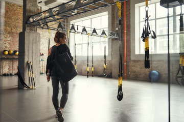 Morning workout. Back view of young athletic woman carrying her sport bag and looking aside while...