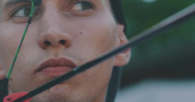 Slow motion close up of young man with professional equipment is practising archery with a bow in a woods in a sunny day. 
