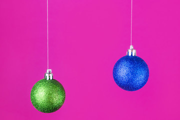 A bright New Year concept - blue and green Christmas balls hanging on a pink background. Place for text, minimalism.