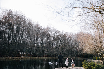 happy beautiful family feeding swans and walking by the lake on autumn day.