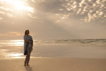 Senior woman wrapped in a shawl standing on the beach