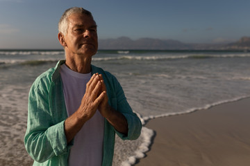 Senior man praying with eyes closed on the beach