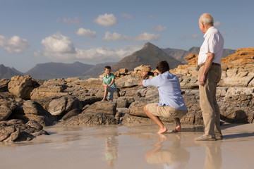 Father clicking photo of his son with mobile phone on beach