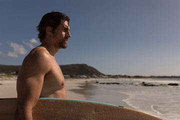 Young male surfer with surfboard standing on beach