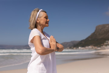 Side view of senior woman meditating in prayer position at beach