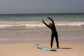 Rear view senior female surfer with surfboard exercising on the beach