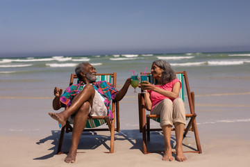 Senior couple relaxing on sun lounger and toasting cocktail glasses on beach