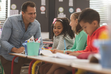 Surface level view of a teacher interacting with school kids while sitting in classroom 