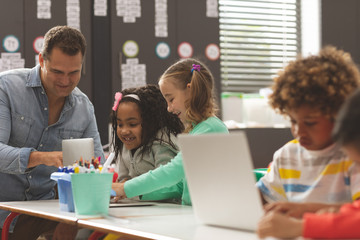 School boys using laptop in classroom while teacher discussing with them