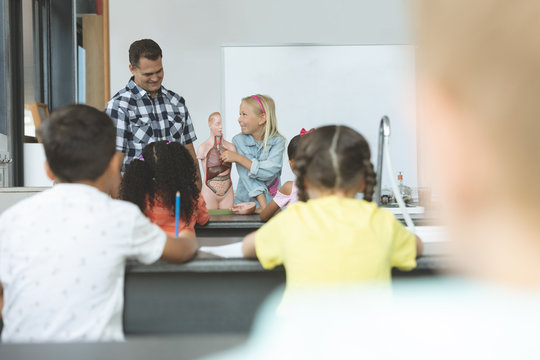  Caucasian schoolgirl explaining to others school kids the human body with his teacher next to her