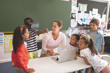 Schoolboy using virtual reality headset at school in classroom with his classmates and her teacher n