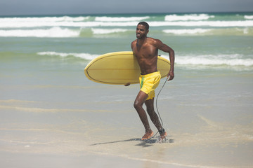 Male surfer with a surfboard running on a beach