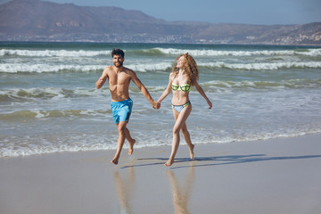 Couple holding hands and running at beach