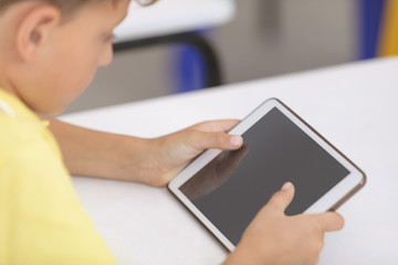 Schoolboy using digital tablet at desk in classroom