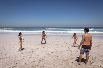 Group of friends playing with Frisbee on beach in the sunshine