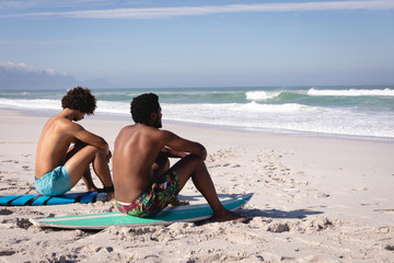 Young men sitting on surfboard at beach in the sunshine