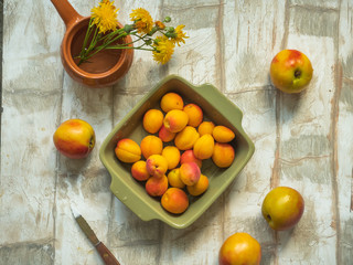 A set of nectarine and apricot fruits in a deep olive square plate on a light table, taken from the top view, a small vase with yellow meadow flowers