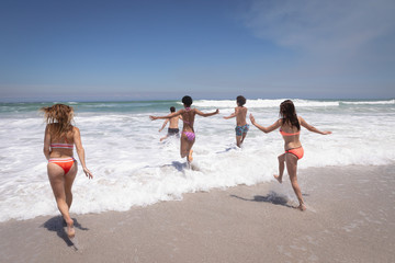Fototapeta premium Group of friends running in ocean waves 