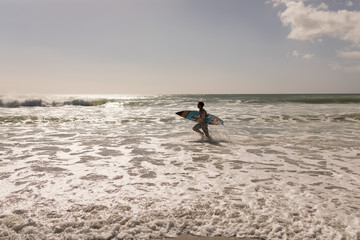 Young male surfer with surfboard running on beach