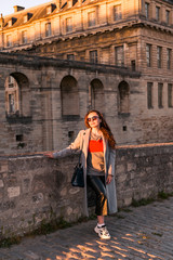 Fototapeta na wymiar The girl near the old castle in France. Vincennes Castle in the rays of the sun at sunset. Travel and tourism.