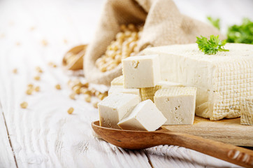 Soy Bean curd tofu on cutting board and in hemp sack on white wooden kitchen table. Space for text