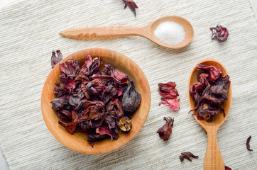 Top view at wooden bowl and spoon of dry hibiscus petals on linen cloth background