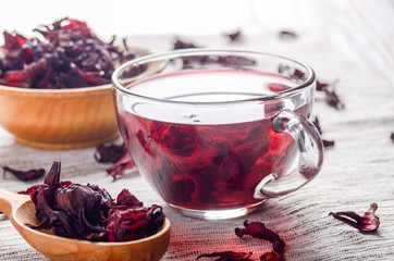 Closeup view at wooden bowl tea cup and spoon of dry hibiscus petals on linen cloth background