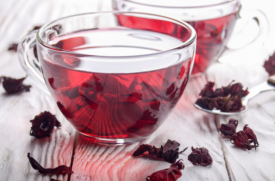 Closeup view at two tea cups and dry hibiscus petals on white wooden table background