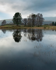 Fototapeta na wymiar Stunning landscape image of dramatic storm clouds over Kelly Hall Tarn in Lake District during late Autumn Fall afternoon
