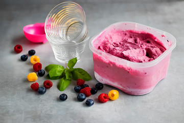 Homemade fresh berry ice cream with basil in a plastic box on a gray background.