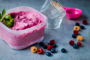 Homemade fresh berry ice cream with basil in a plastic box on a gray background.