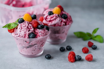 Homemade ice cream made from fresh berries with basil in glass bowl on a gray background.