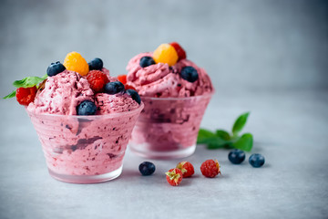 Homemade ice cream made from fresh berries with basil in glass bowl on a gray background.