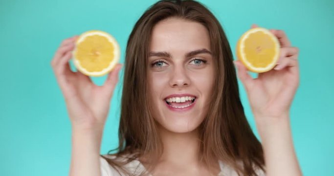 Yong girl covers her face with lemon. Girl dabbles and laughsTurquoise background.
