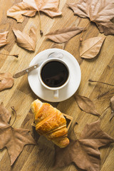 Leaves around coffee and croissant