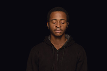 Close up portrait of young african-american man isolated on black studio background. Real emotions of male model with eyes closed, looks calm. Facial expression, human nature and emotions concept.