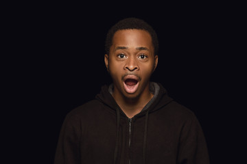 Close up portrait of young african-american man isolated on black studio background. Real emotions of male model. Looks astonished and shocked. Facial expression, human nature and emotions concept.