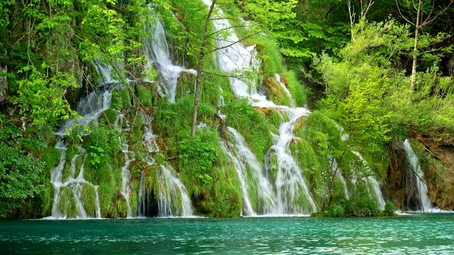 Lovely waterfall with many cascades, surrounded by rich green flora, flowing into a turquoise colored lake in Plitvice Lakes National Park, Croatia. 4K