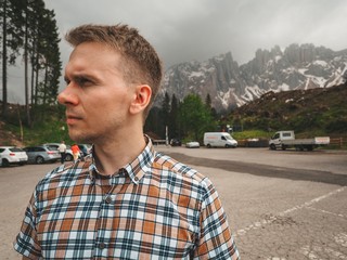 A young man in a plaid shirt stands against the background of the Dolomites. Mountain summer landscape in the Dolomites in Northern Italy.