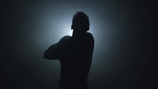 Handsome boy after training, wipes sweat, silhouette on black background