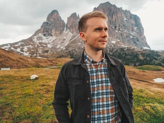 Naklejka premium A young man in a plaid shirt stands against the background of the Dolomites. Mountain summer landscape in the Dolomites in Northern Italy.