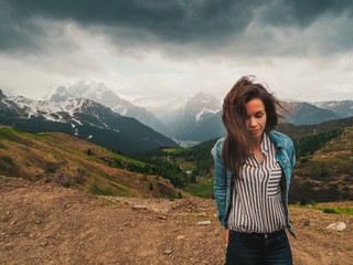 Naklejka premium A brunette girl with long hair fluttering in the wind stands against the background of the Dolomite mountains. Mountain summer landscape in the Dolomites in Northern Italy.