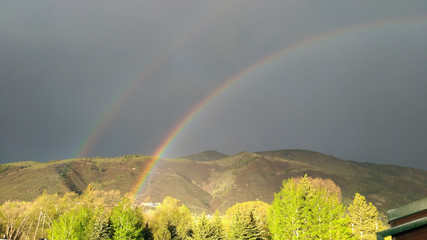 Double rainbows over forest in the front of the dark thunderstorm sky