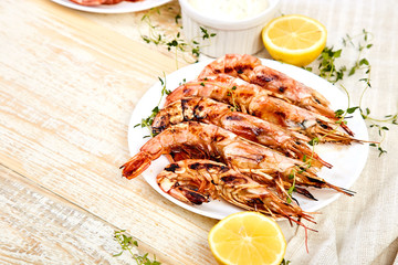 Grilled big tiger shrimps prawns on white plate with spices, lemon, fresh herbs on white wooden background, top view. Grilled seafood. Barbecue shrimps. Copy space.