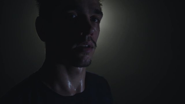 Epic close-up shot of sweaty man. Drop of water on his face macro slow motion. Turning head from dowm to camera