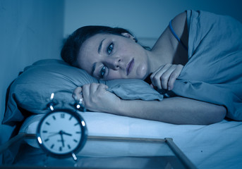 Attractive woman in bed staring at alarm clock trying to sleep feeling stressed and sleepless